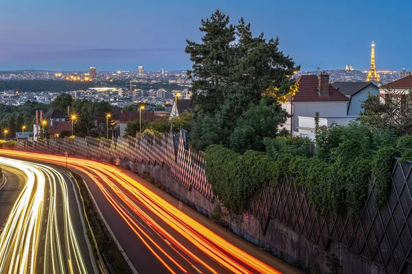 Evening light trails on a road outside Paris, with the Eiffel Tower in the distance